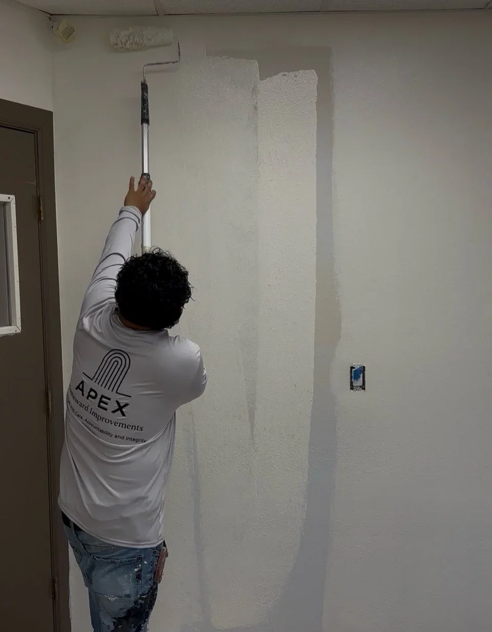 Painter using roller to apply white primer or paint to interior drywall wall