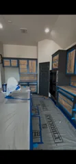 Interior room with white painted ceiling and walls, blue painter's tape on trim, protective coverings on floor