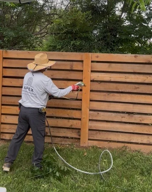 Worker applying stain to horizontal wood fence panels with spray equipment