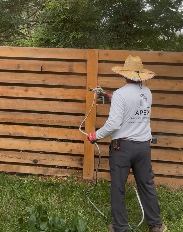 Worker spray-staining horizontal wood fence panels with protective coating
