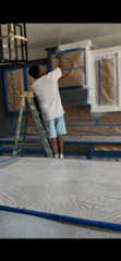 Painter on ladder applying ceiling paint with roller extension pole
