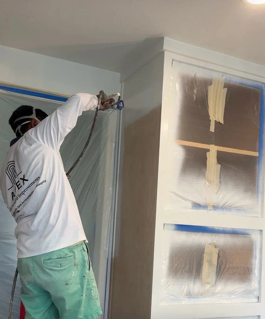 Painter applying primer to drywall with taped windows and protective plastic covering